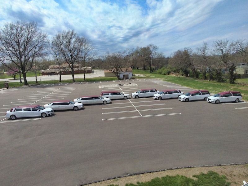 Eight white limousines parked in a lot under a partly cloudy sky.