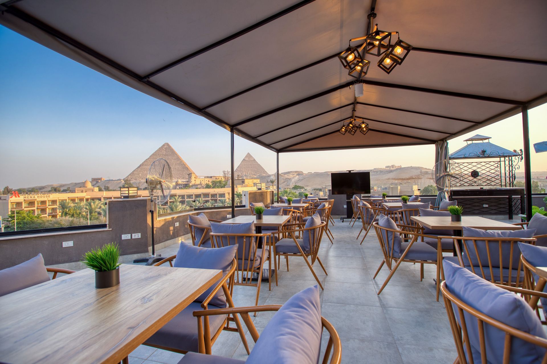 A restaurant with tables and chairs on a rooftop with pyramids in the background.