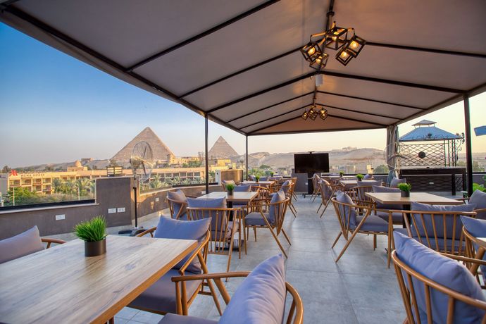 A restaurant with tables and chairs on a rooftop with pyramids in the background.