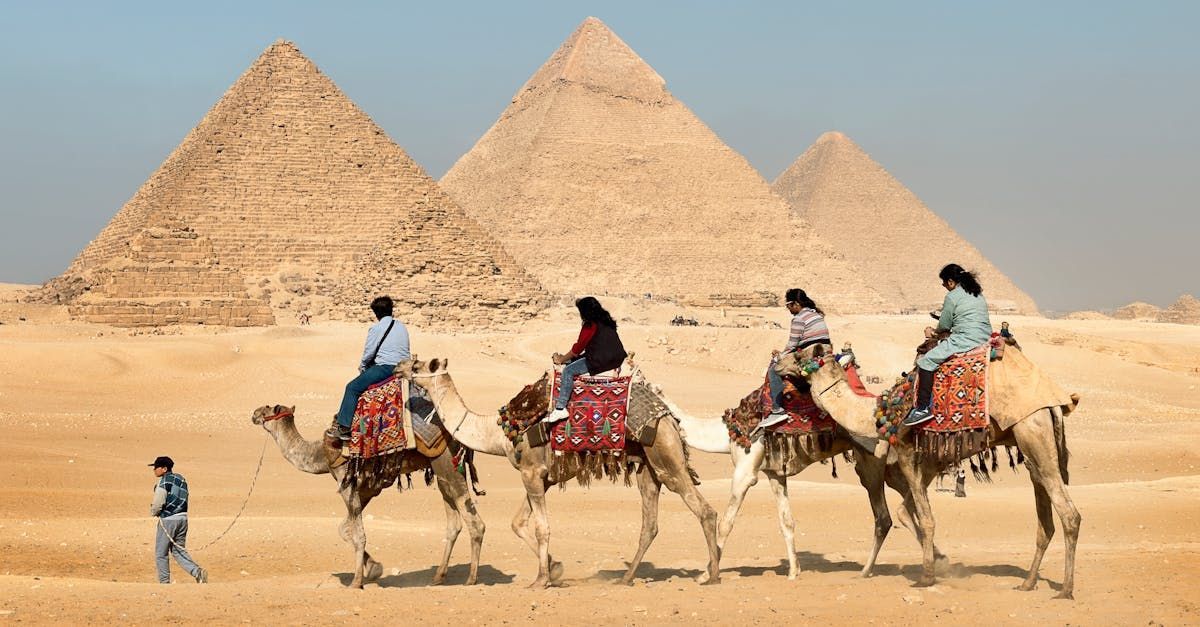 A group of people are riding camels in front of the pyramids.