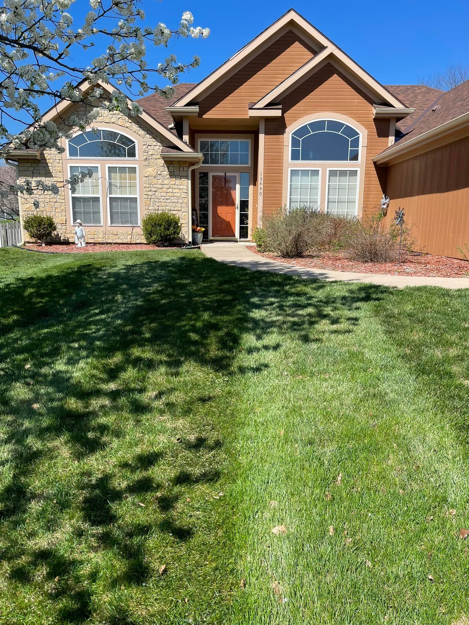 House with brown and stone exterior, arched windows, and a green lawn on a sunny day.