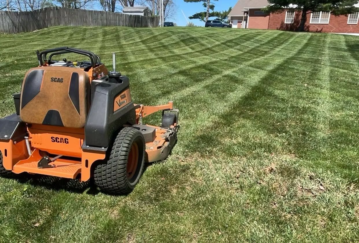 Orange zero-turn mower cutting grass on a sloped lawn, creating striped patterns.