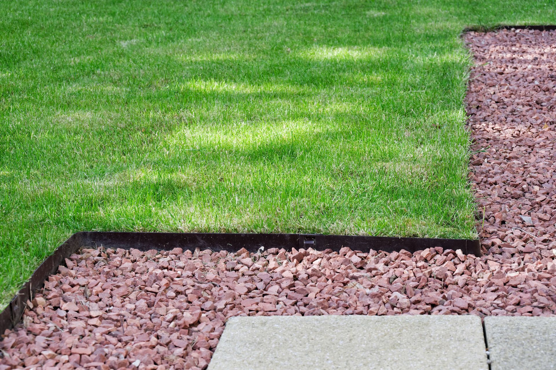 Green lawn bordered by red gravel and a gray stone.