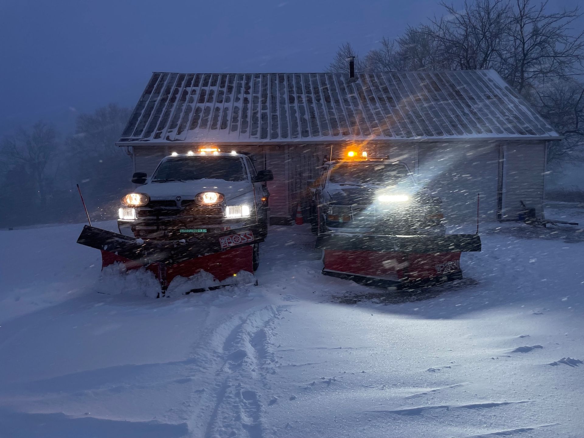 Two snowplow trucks clearing snow in front of a white building at night.