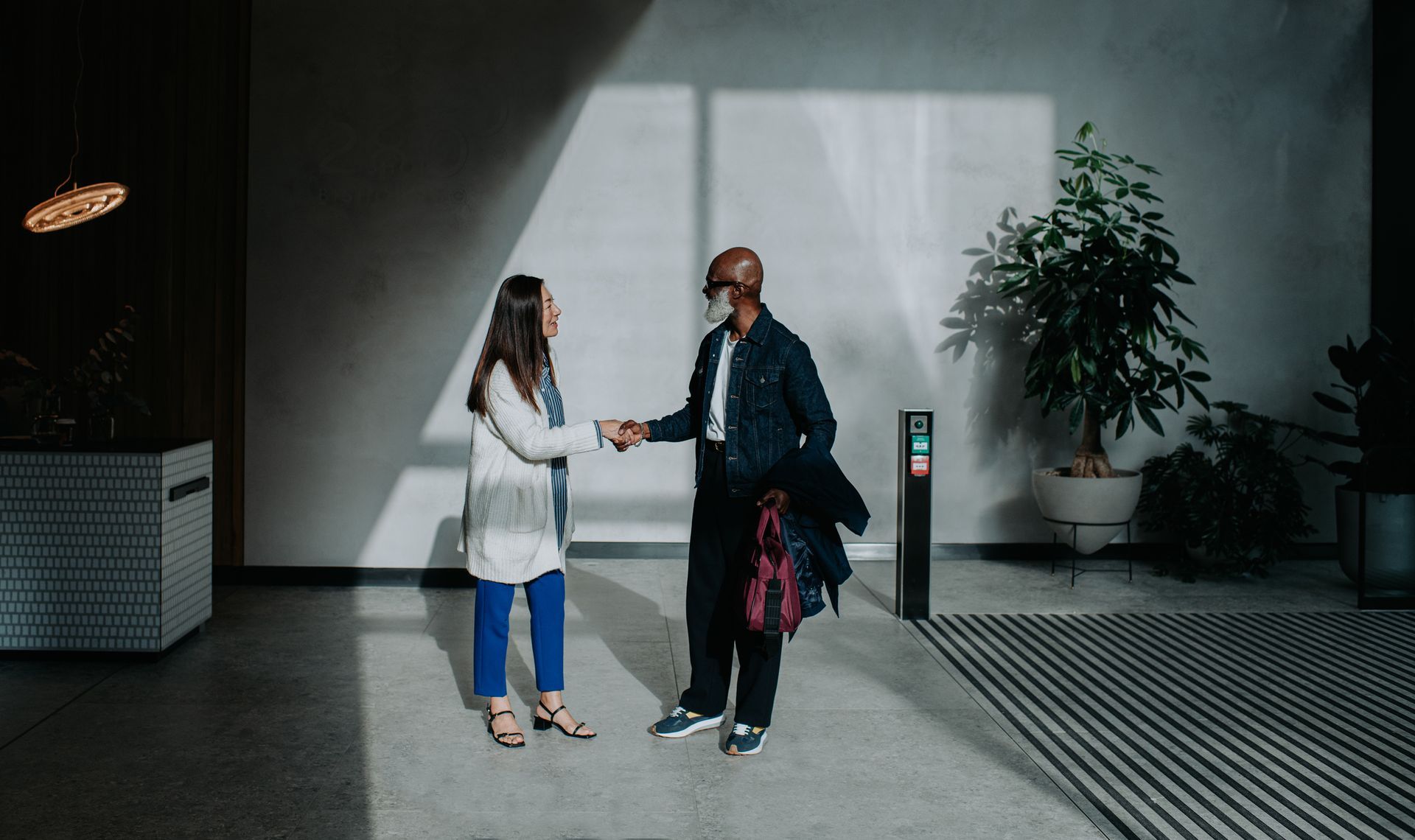 A man and a woman are shaking hands in a lobby.