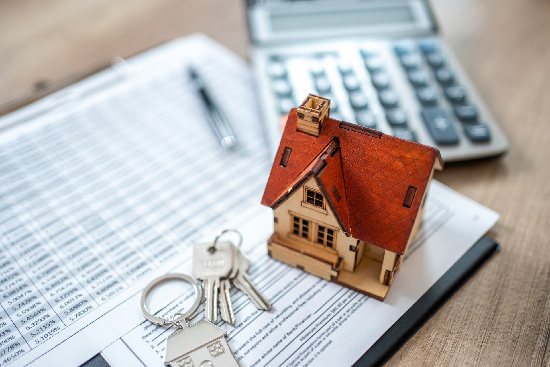 A model house and keys are sitting on top of a clipboard next to a calculator.