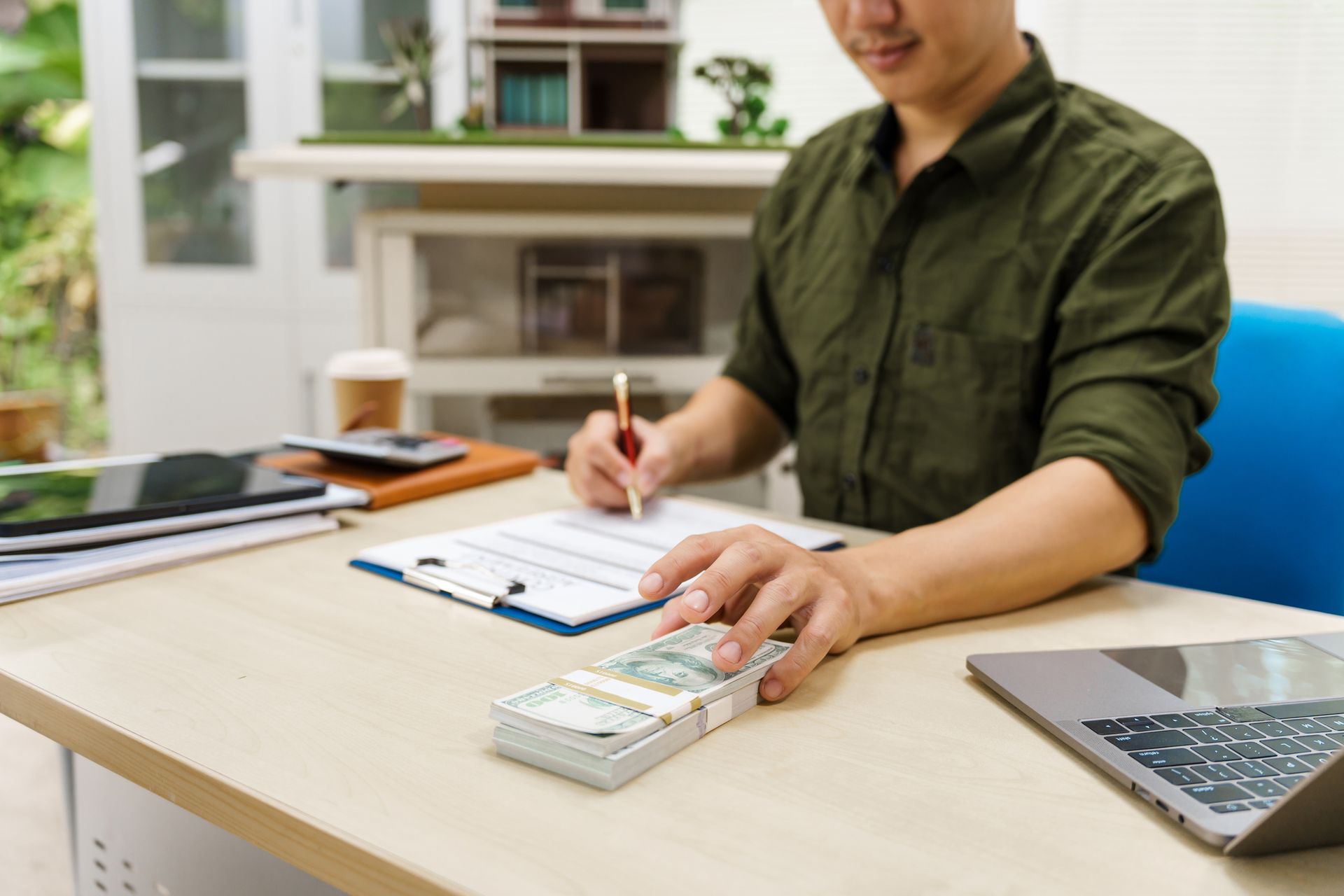 A man is sitting at a desk with a stack of money on it.