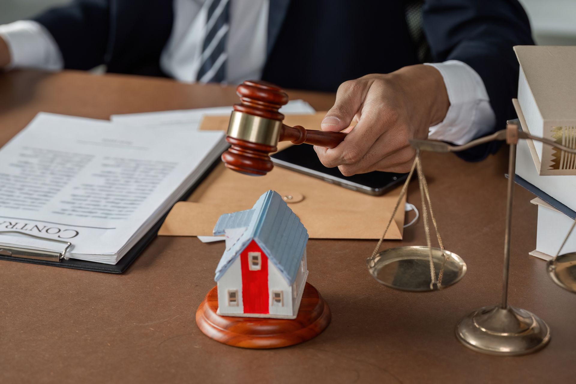 A man is holding a wooden gavel over a model house.