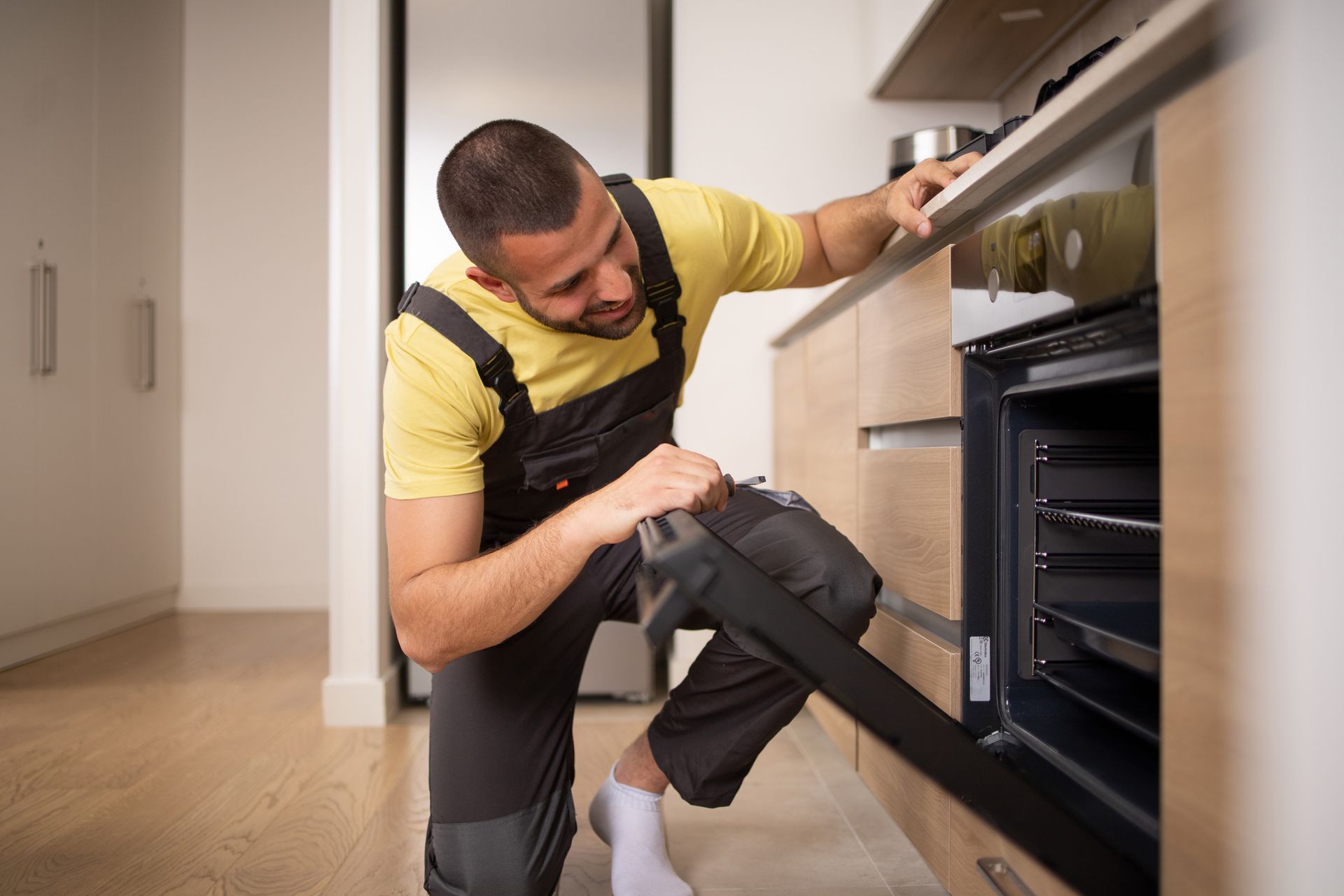 A man fixing an oven in a kitchen, showcasing oven repair skills with professional tools.
