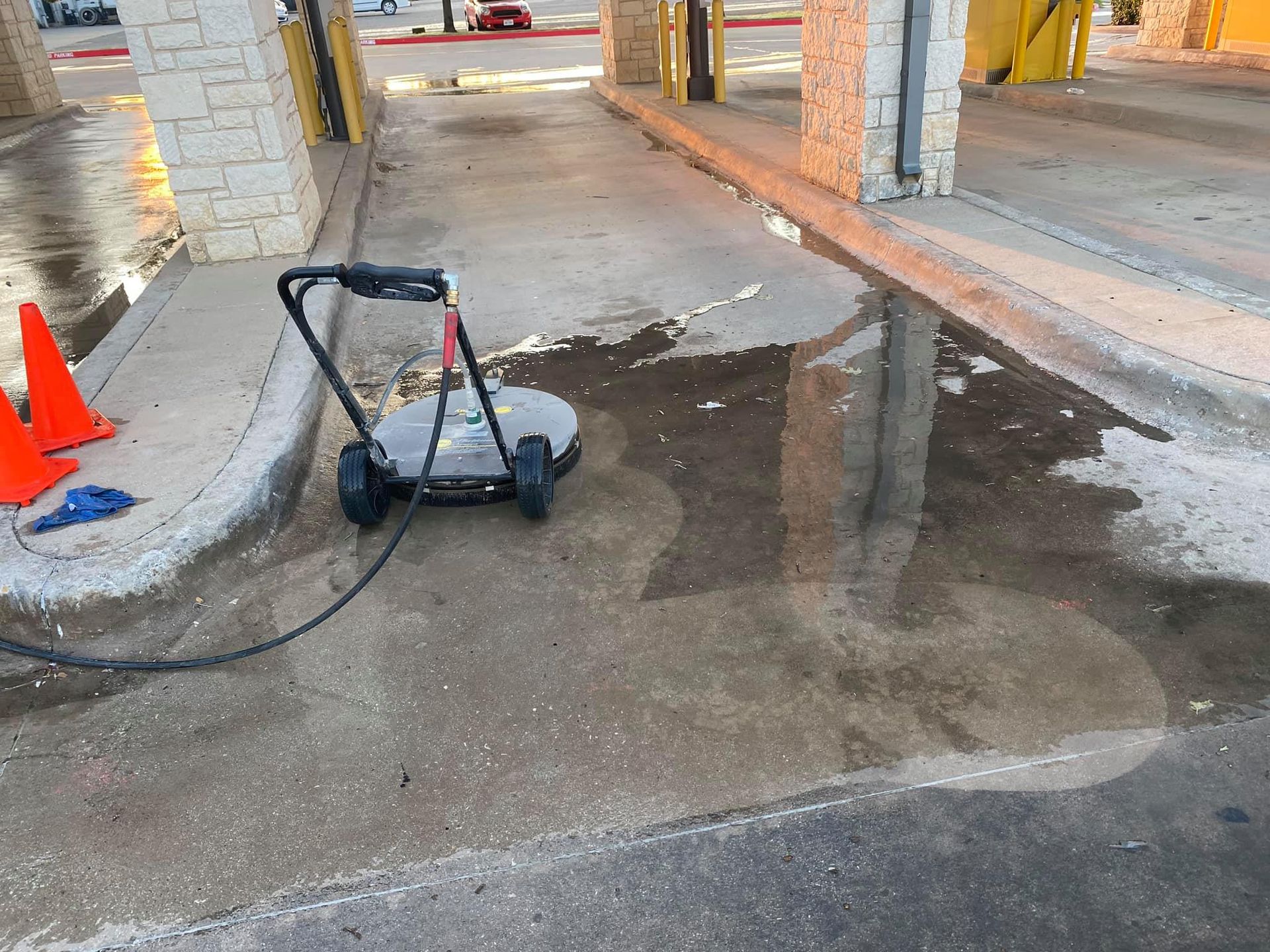 A person uses a surface cleaner to wash a wet concrete drive-through at a bank.