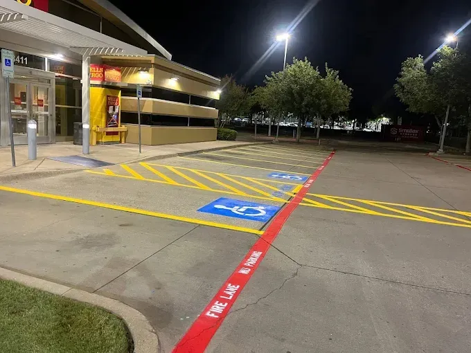 Exterior of a building at night with handicap parking spots and a fire lane. Red and yellow paint on concrete.