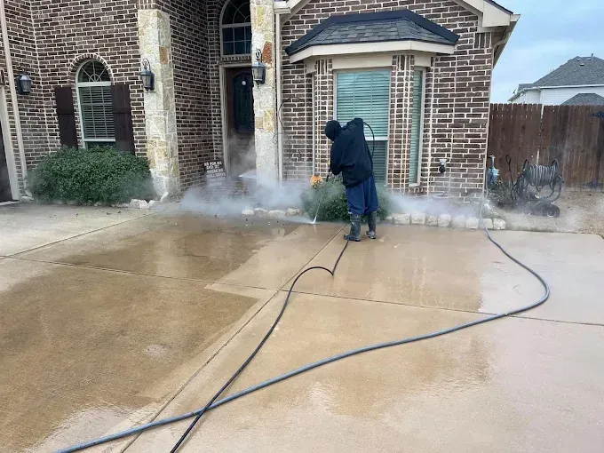 Person pressure washing a driveway in front of a brick house.