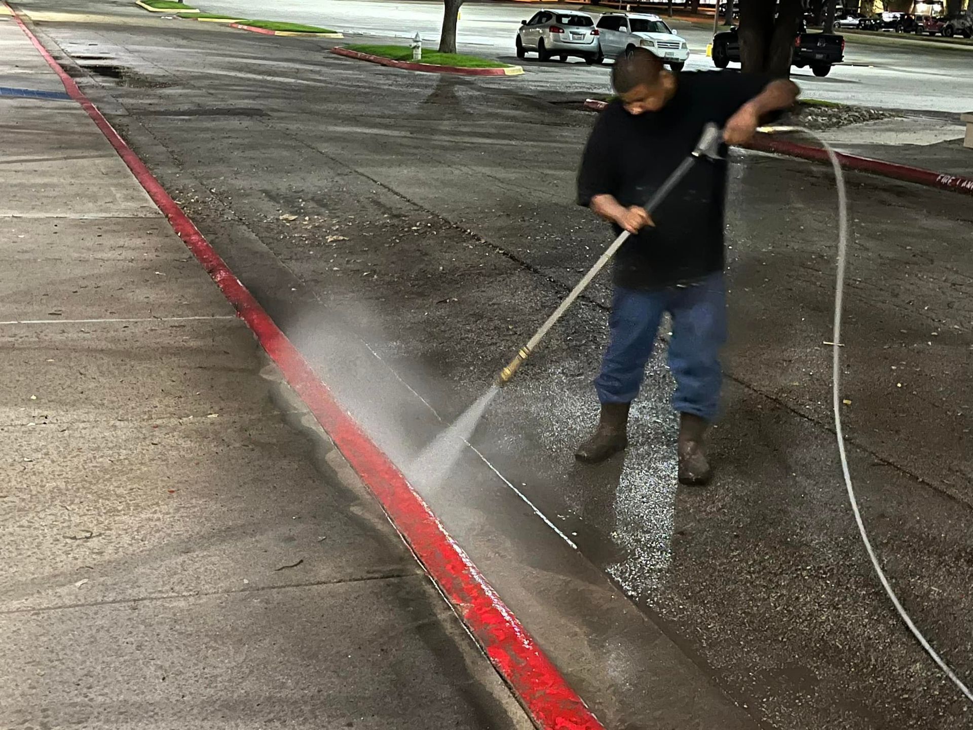 Man power washing a red painted curb on asphalt road.