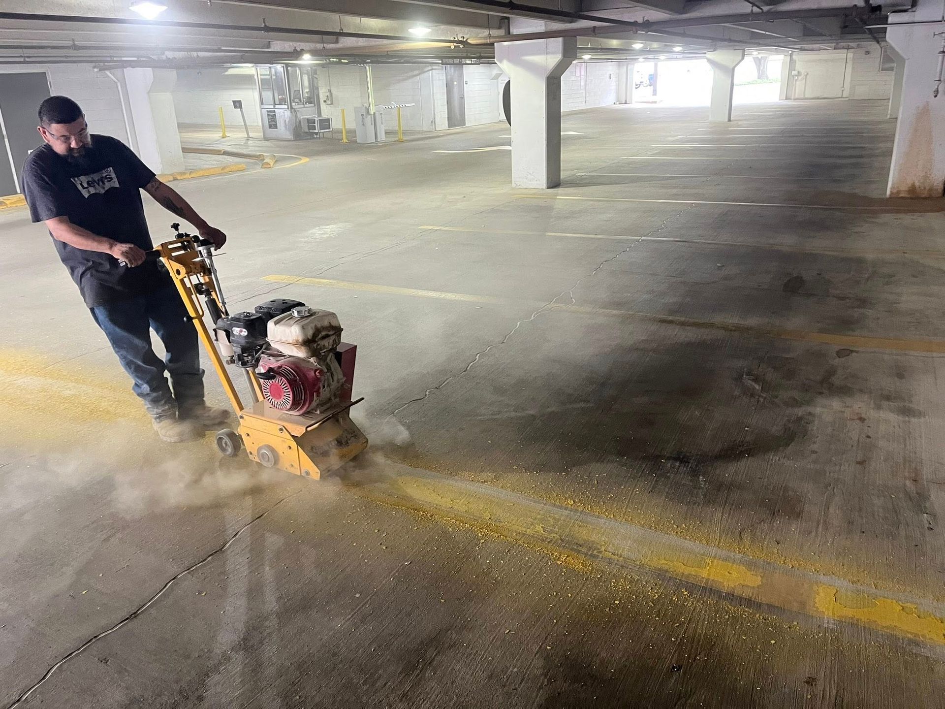 Man using a grinder to remove yellow line markings in a parking garage. Dust is visible.