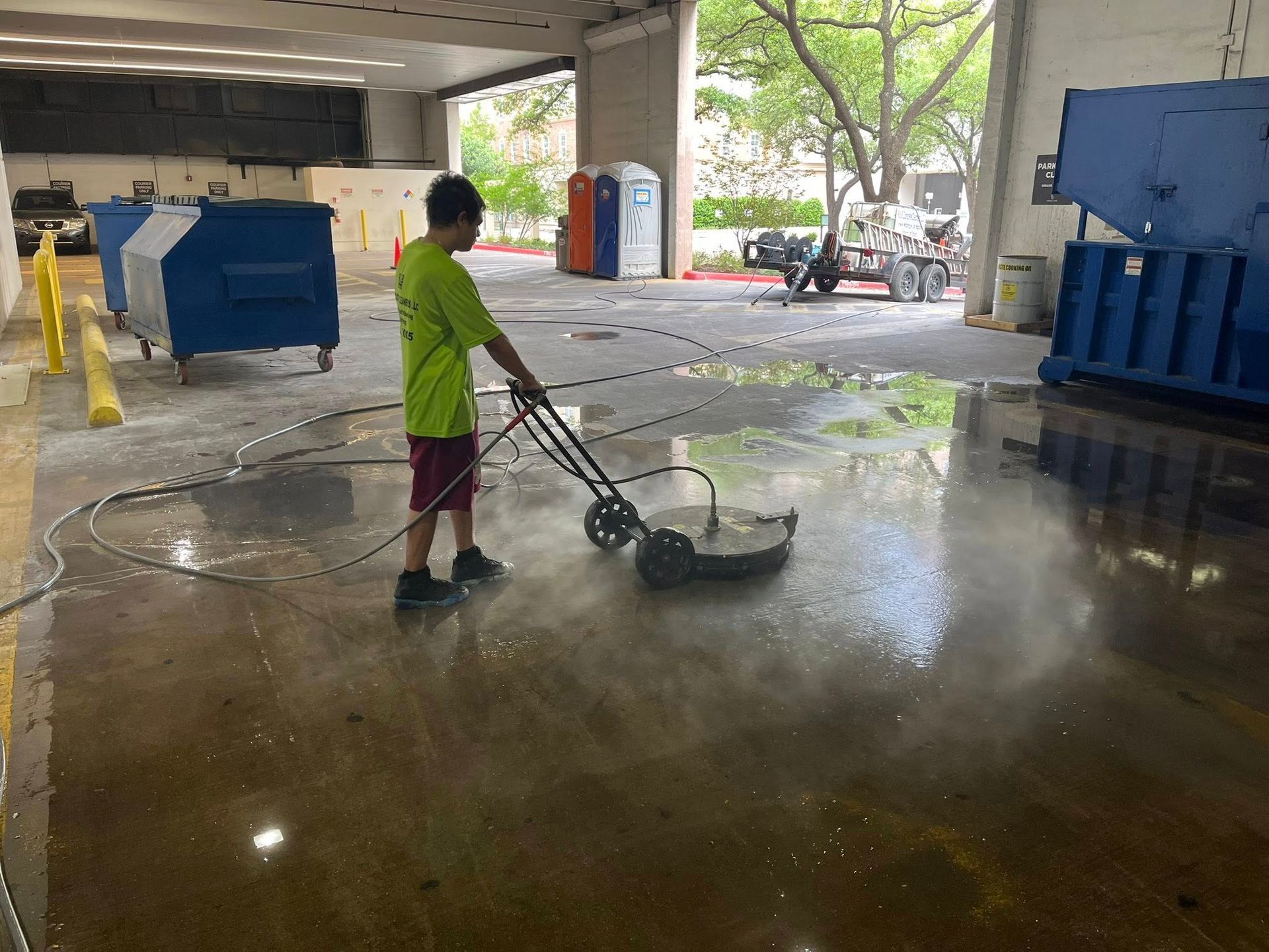 Boy pressure washing a concrete floor in an outdoor parking area.