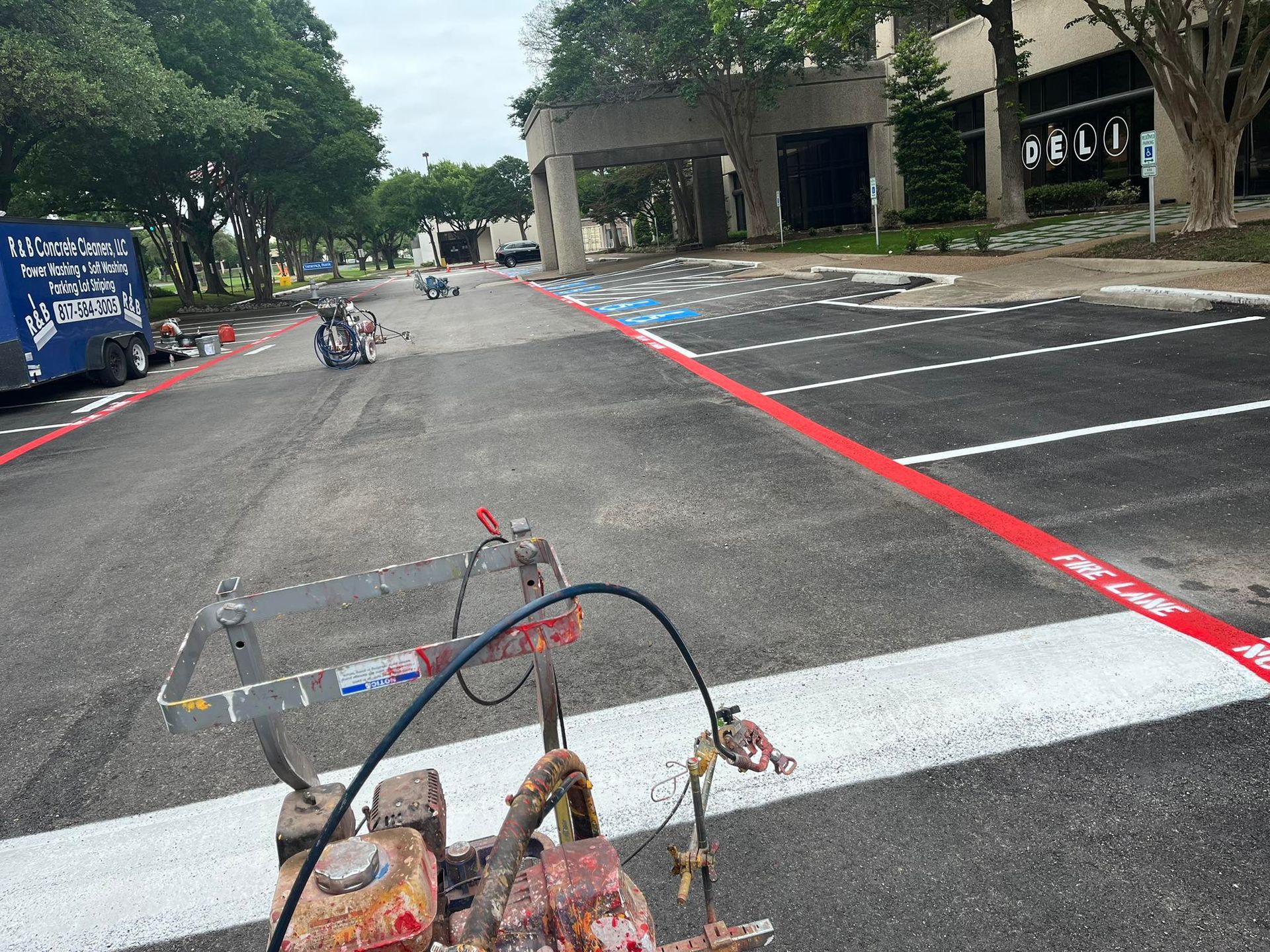 Parking lot striping with red and white paint. Striping machine in foreground, finished lines visible.