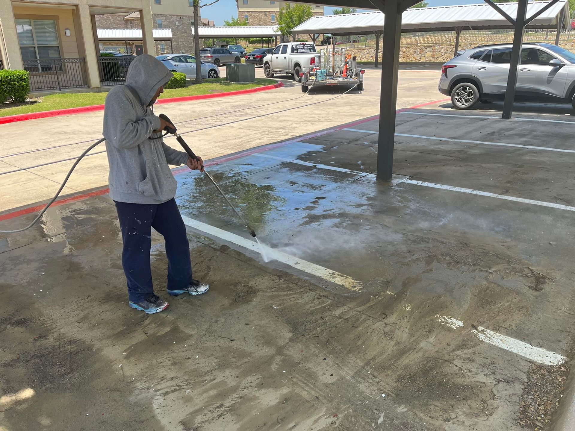 Person power washing a parking spot; gray hoodie, blue pants, asphalt.