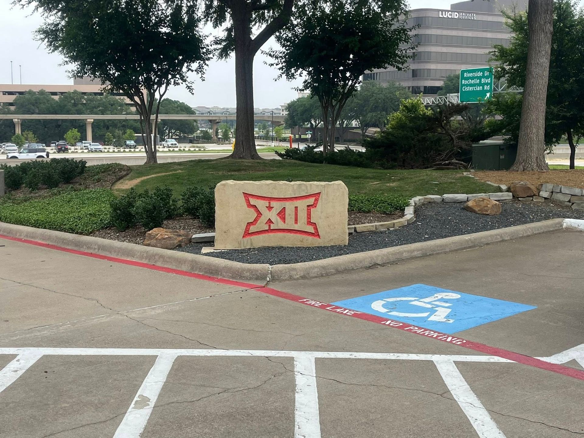 Sign with the Big 12 logo in a parking lot with a handicap parking spot.