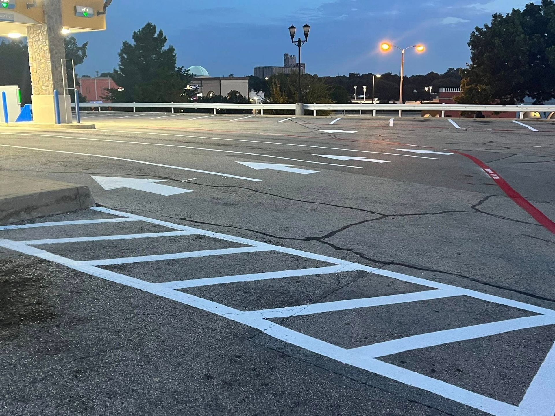 Asphalt parking lot with white lines, an arrow, and a gas station in the background.