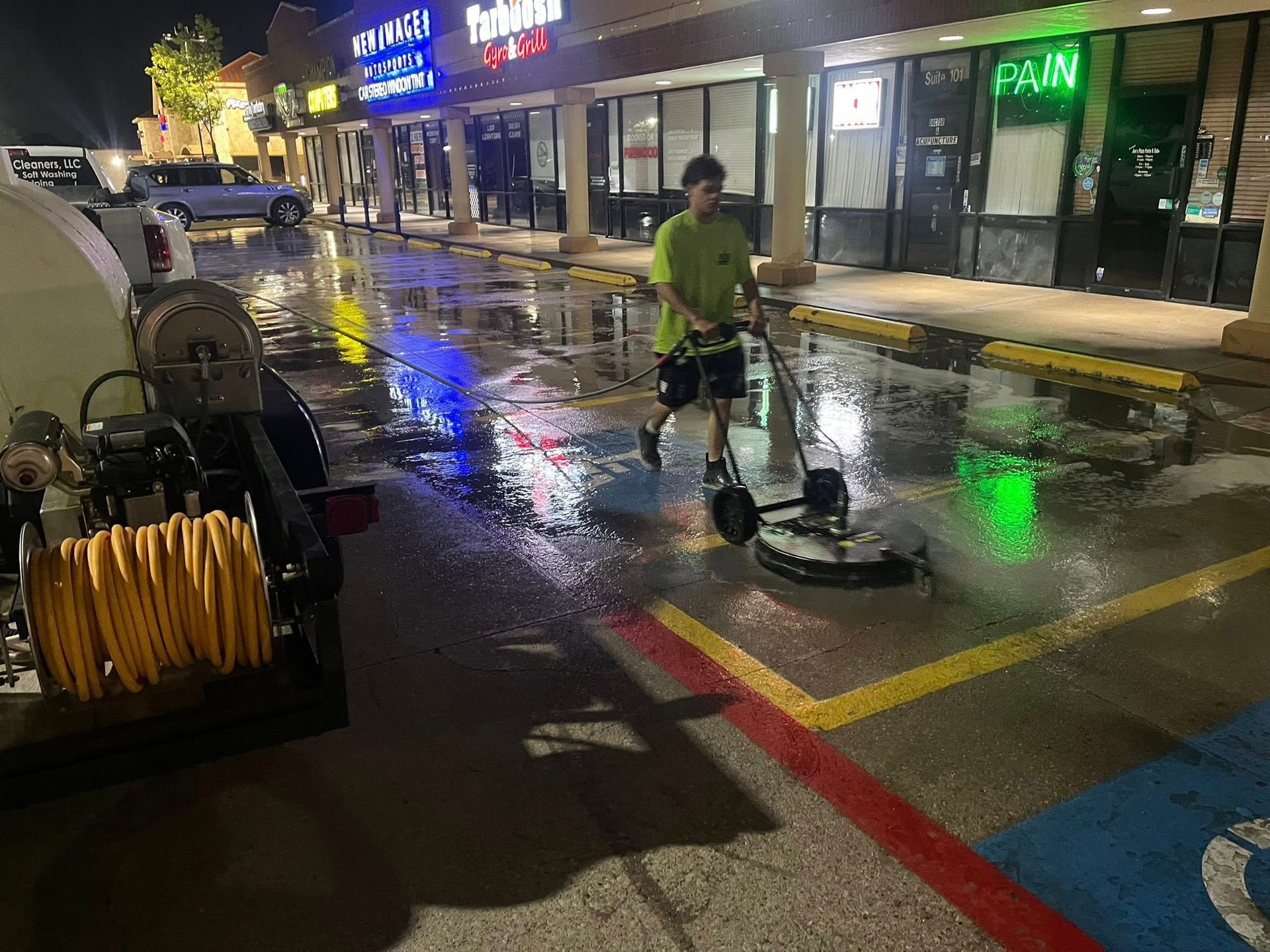 Man using a floor cleaner on a wet commercial parking area at night.