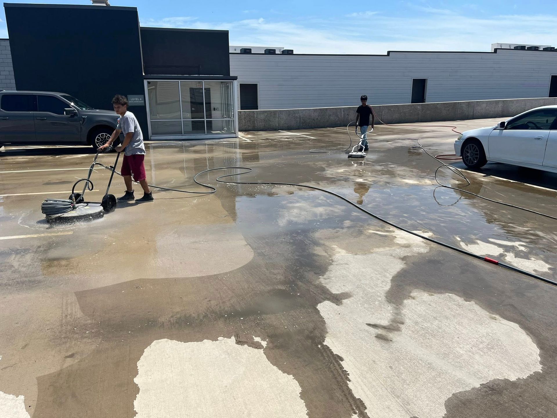 Two people using pressure washers to clean a concrete rooftop on a sunny day.
