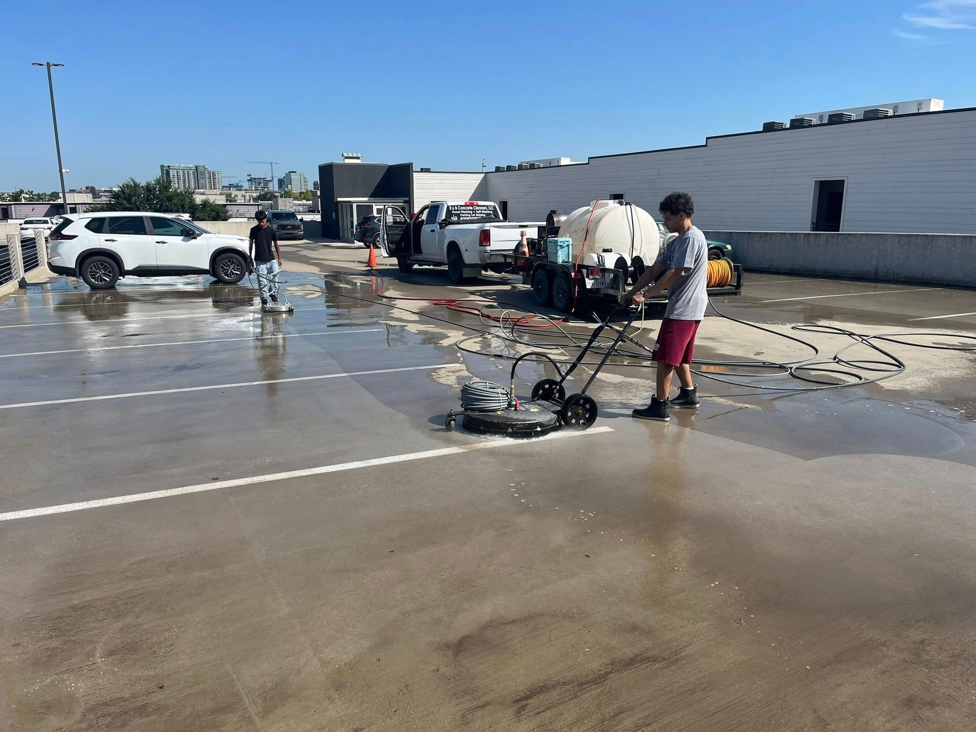 People pressure washing a large concrete area, including a parking lot.