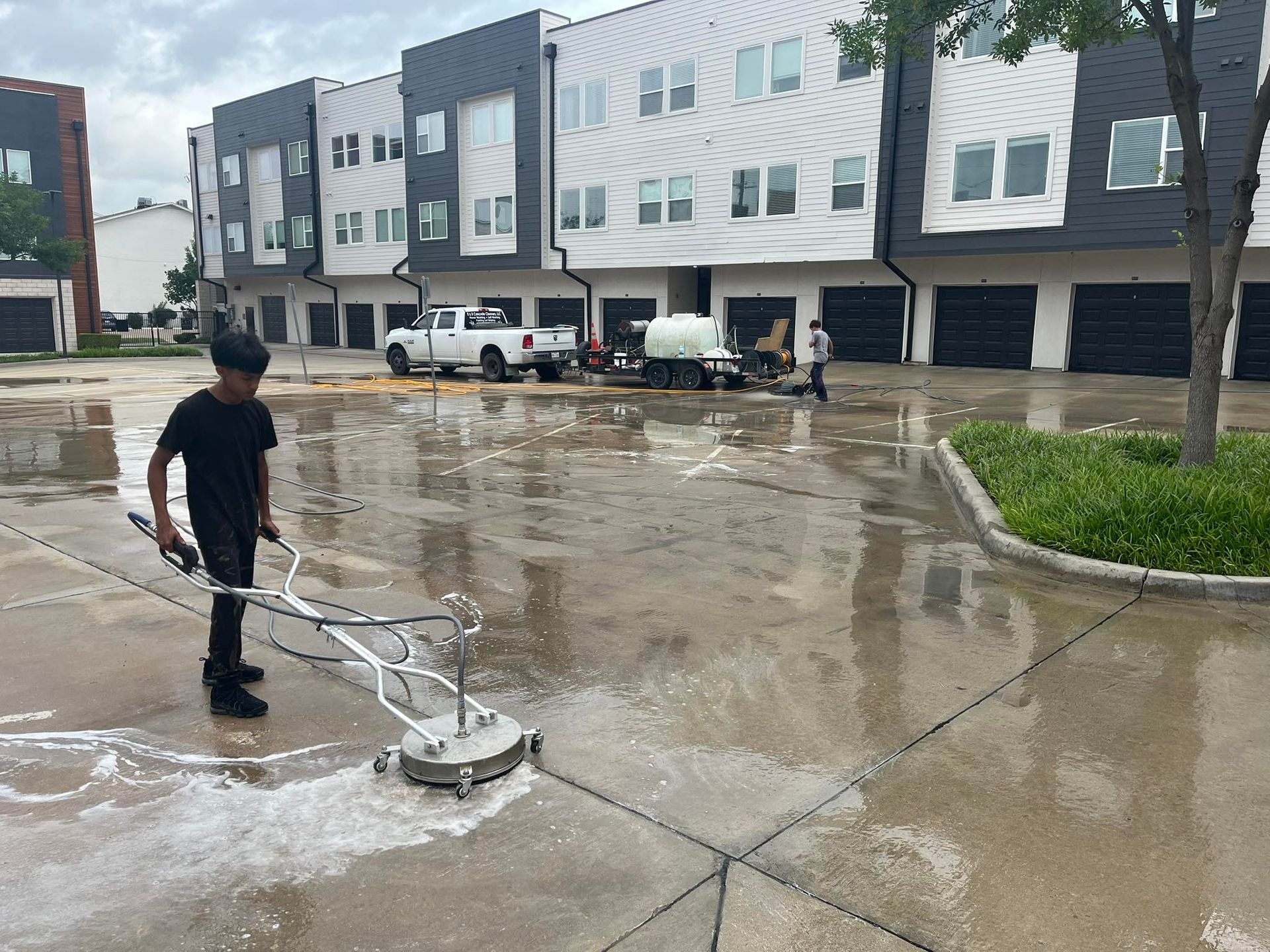 Person pressure washing a concrete surface in front of modern townhouses.