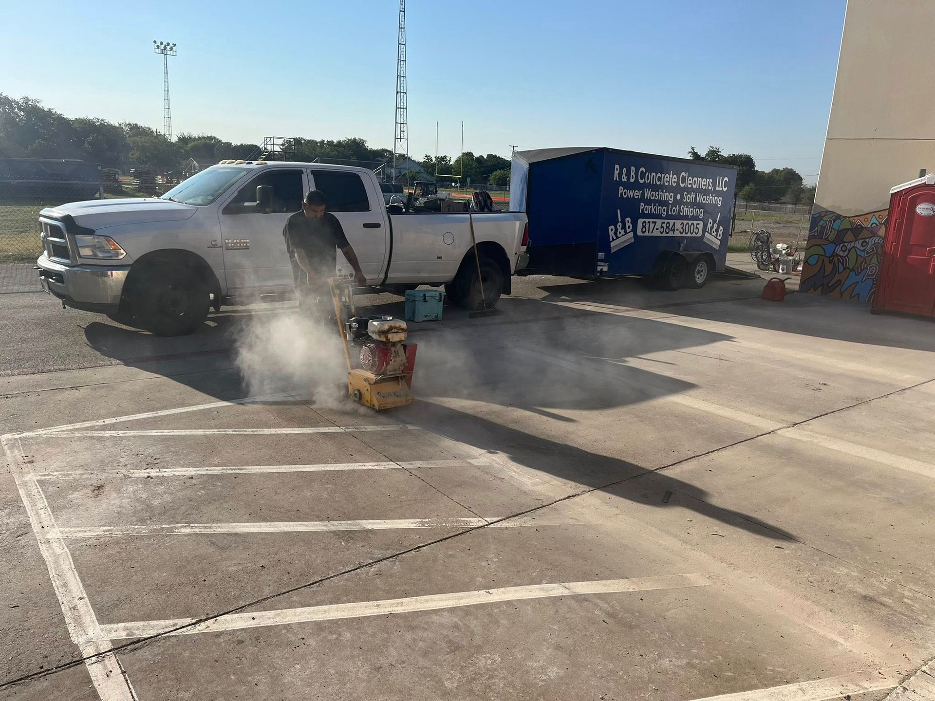 Man using a concrete saw to cut lines on a concrete parking lot. Truck and trailer parked nearby.