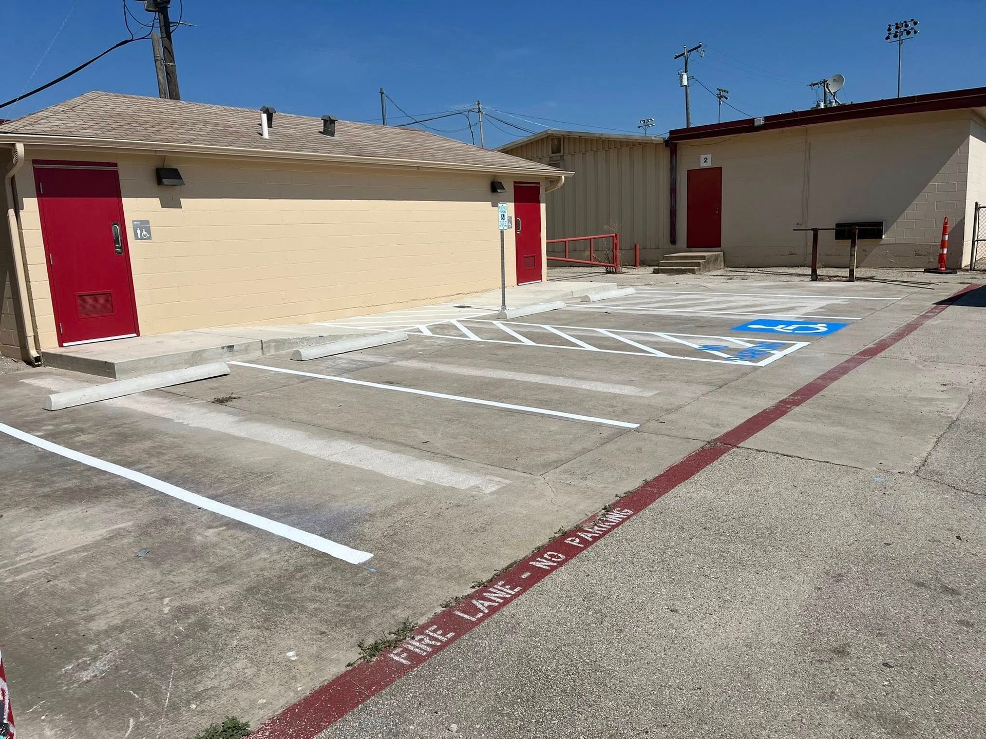 Parking lot with painted spaces, including an accessible space, next to a building with red doors.