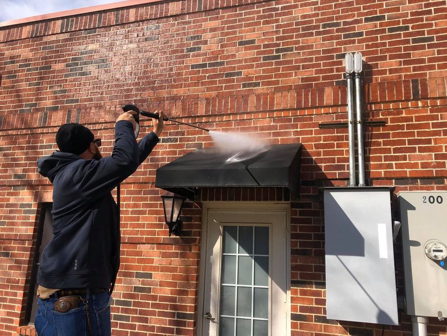 Man pressure washing a brick building, cleaning an awning.