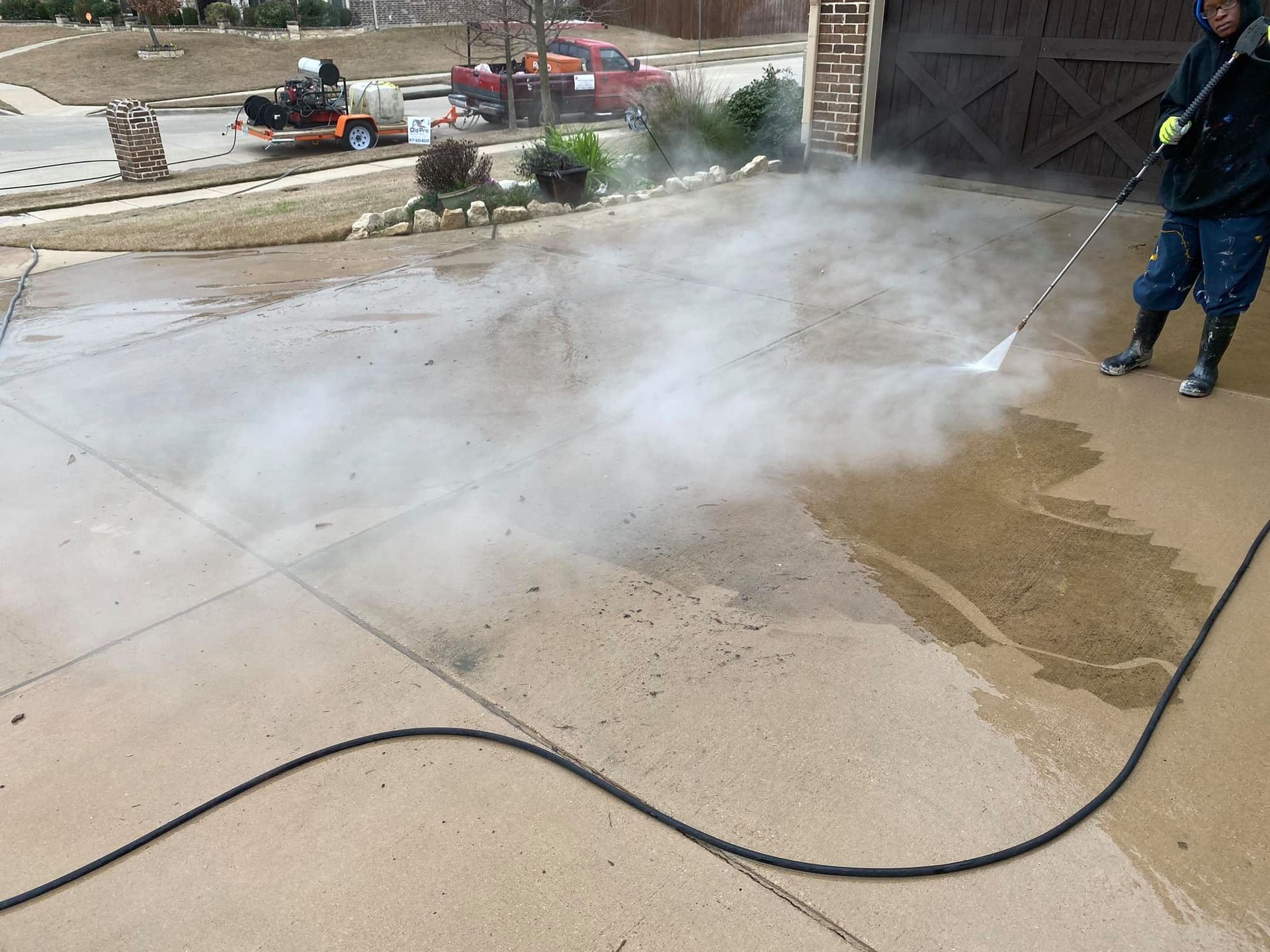 Person power washing a concrete driveway, creating steam. A truck is visible in the background.