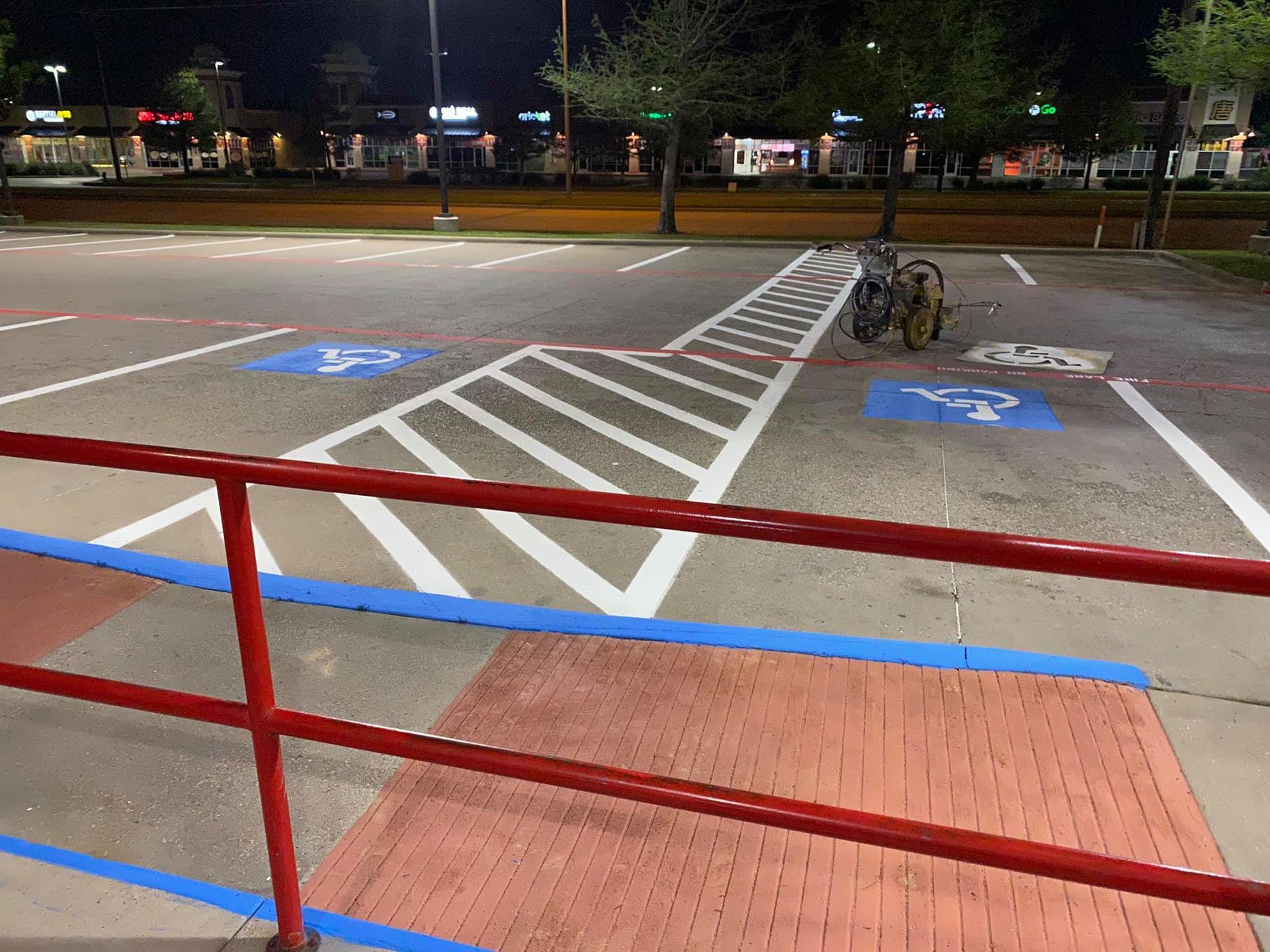 Red and blue railings overlook a parking lot at night. Blue handicap symbols and white parking lines are visible.