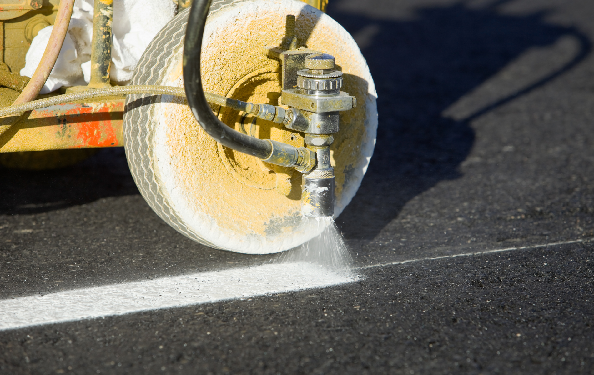 Road marking machine spraying white paint onto asphalt to create a lane line.