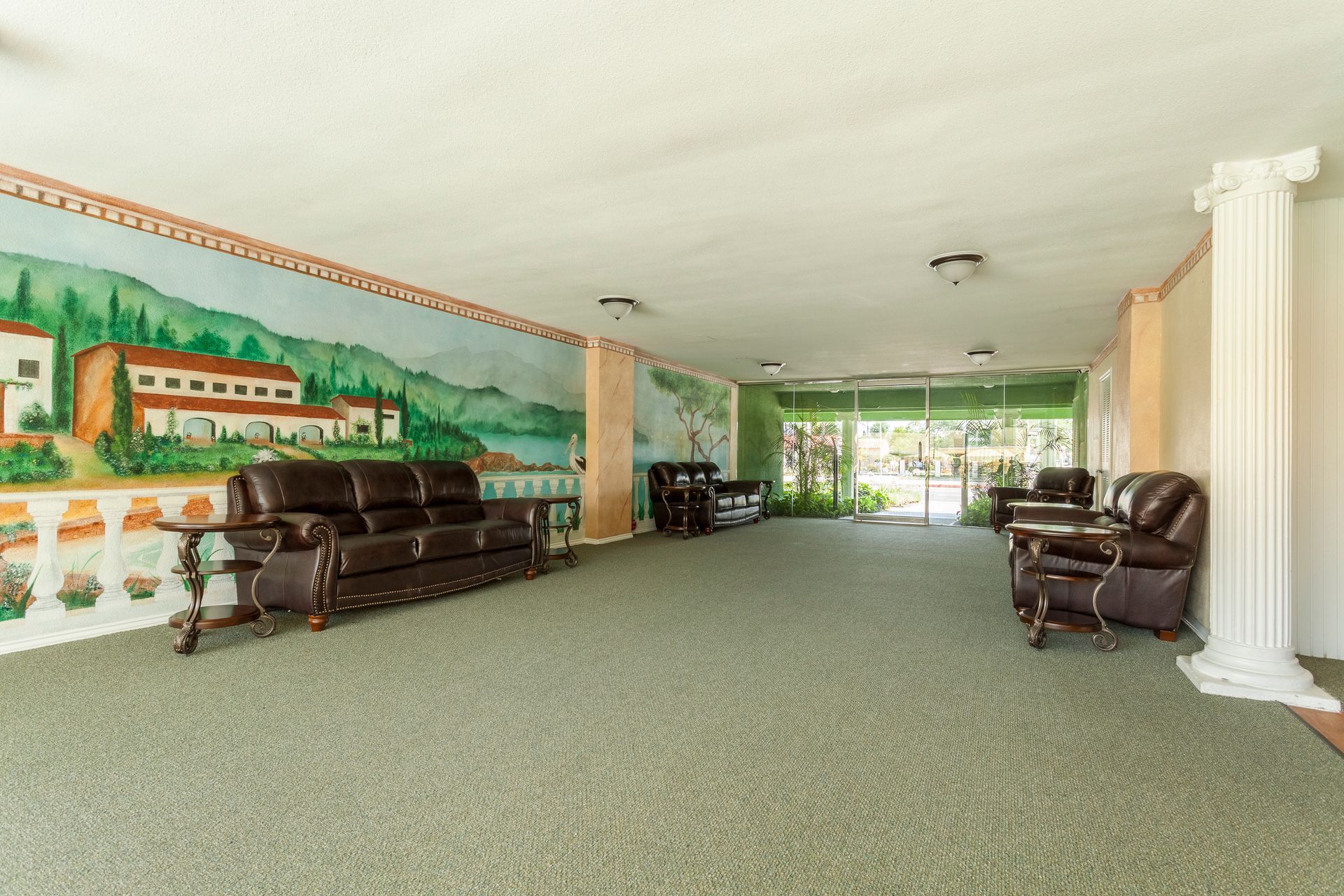 A large room with a couch , chairs , tables and a painting on the wall.