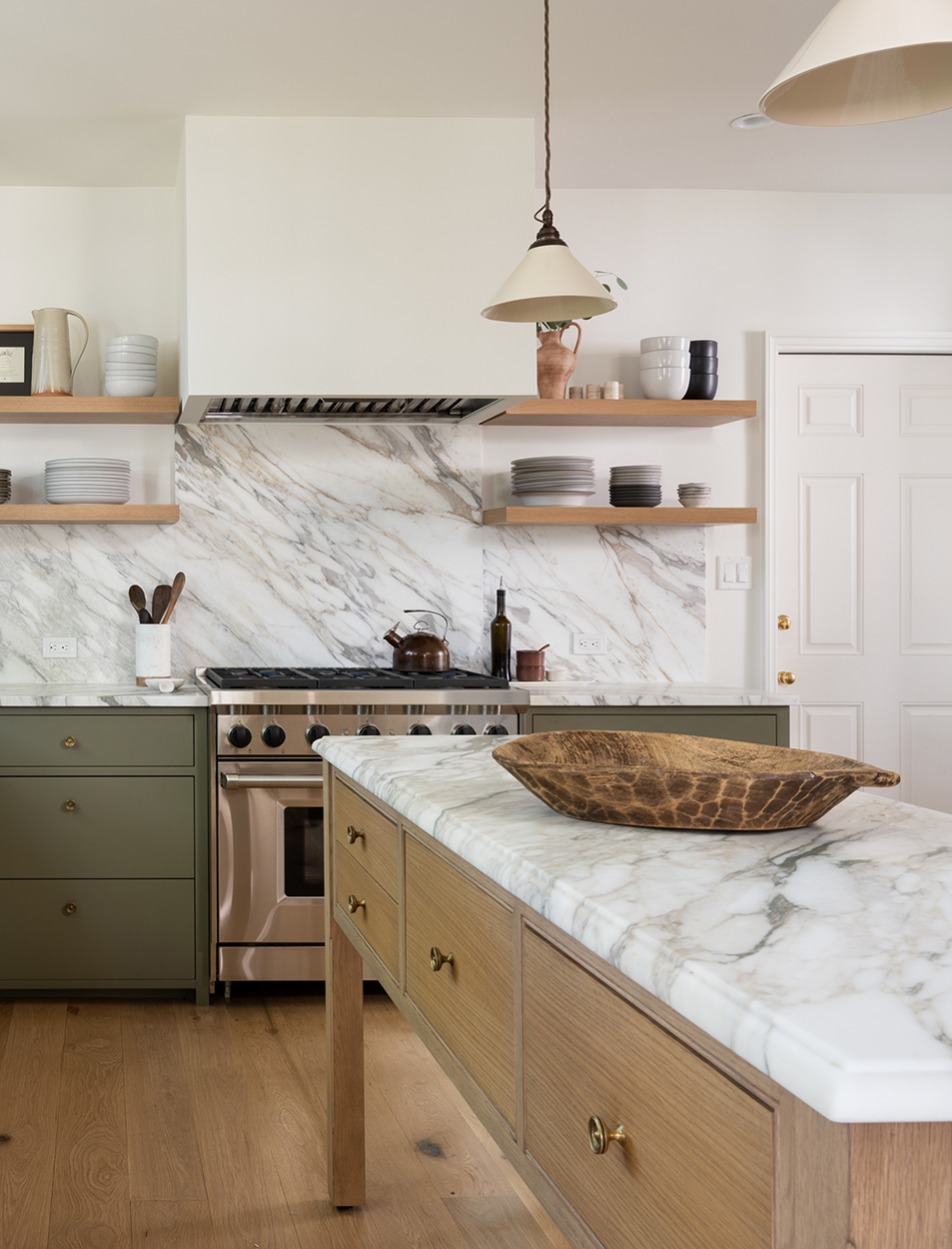 A kitchen with marble counter tops , green cabinets , a stove and a bowl on the counter.