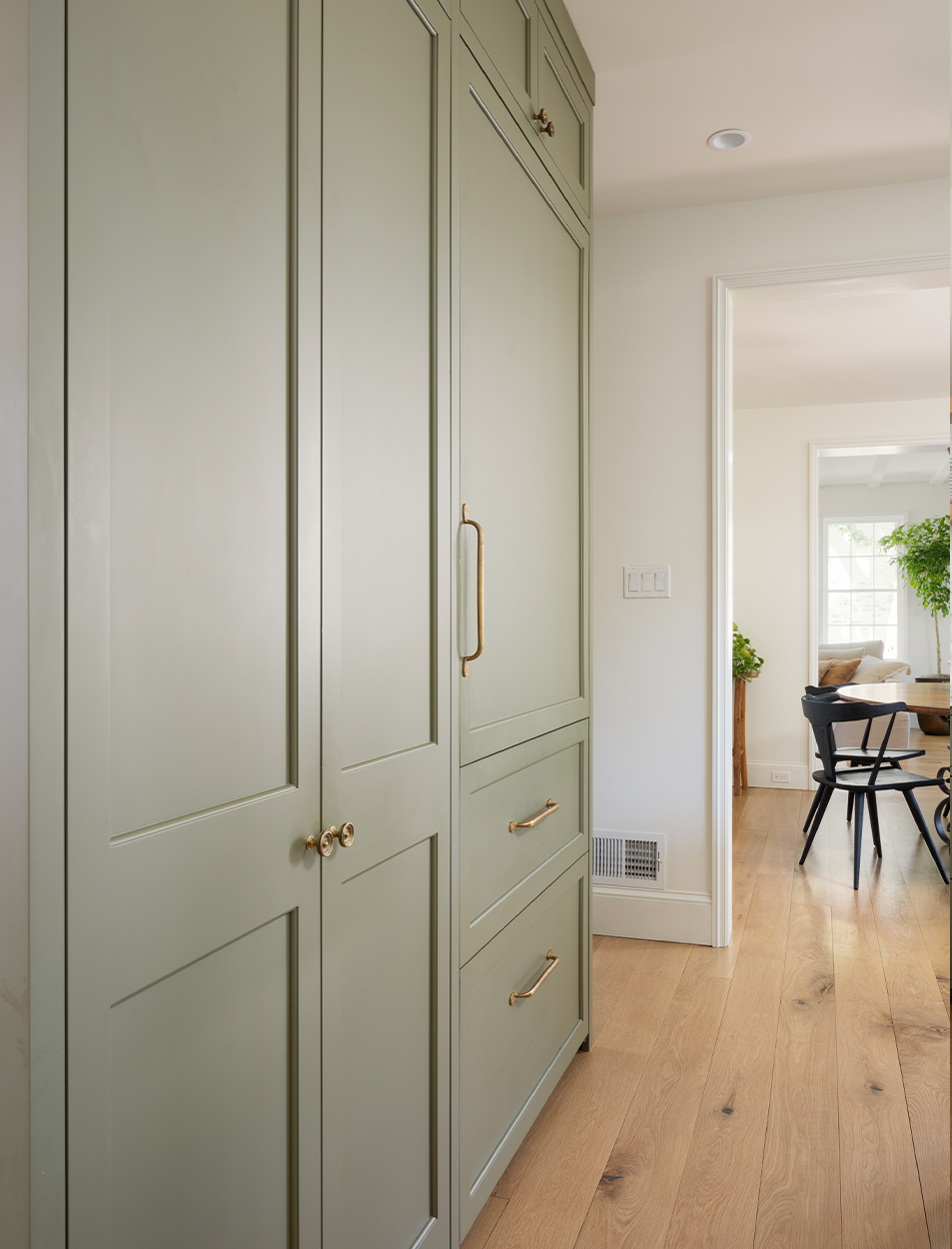 A hallway with green cabinets and drawers leading to a dining room.