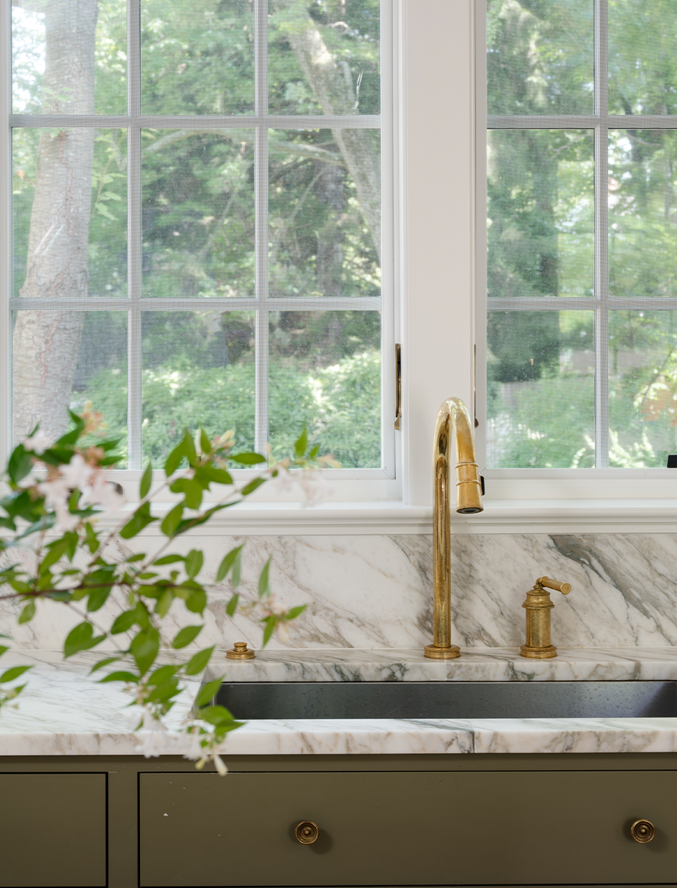 A kitchen sink with a marble counter top and a brass faucet.