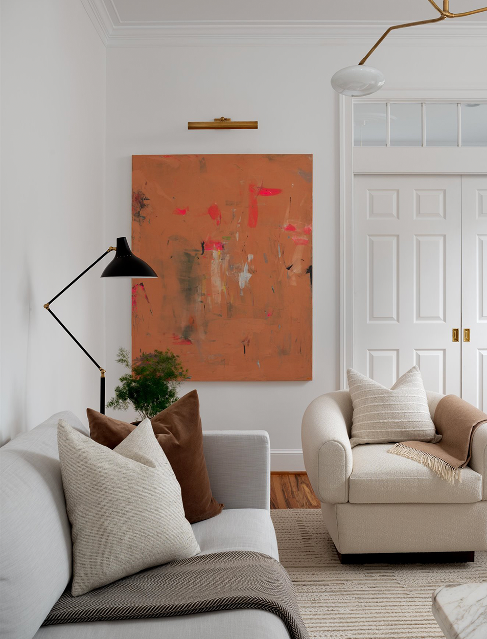 A living room with a couch , chair , lamp and painting on the wall.