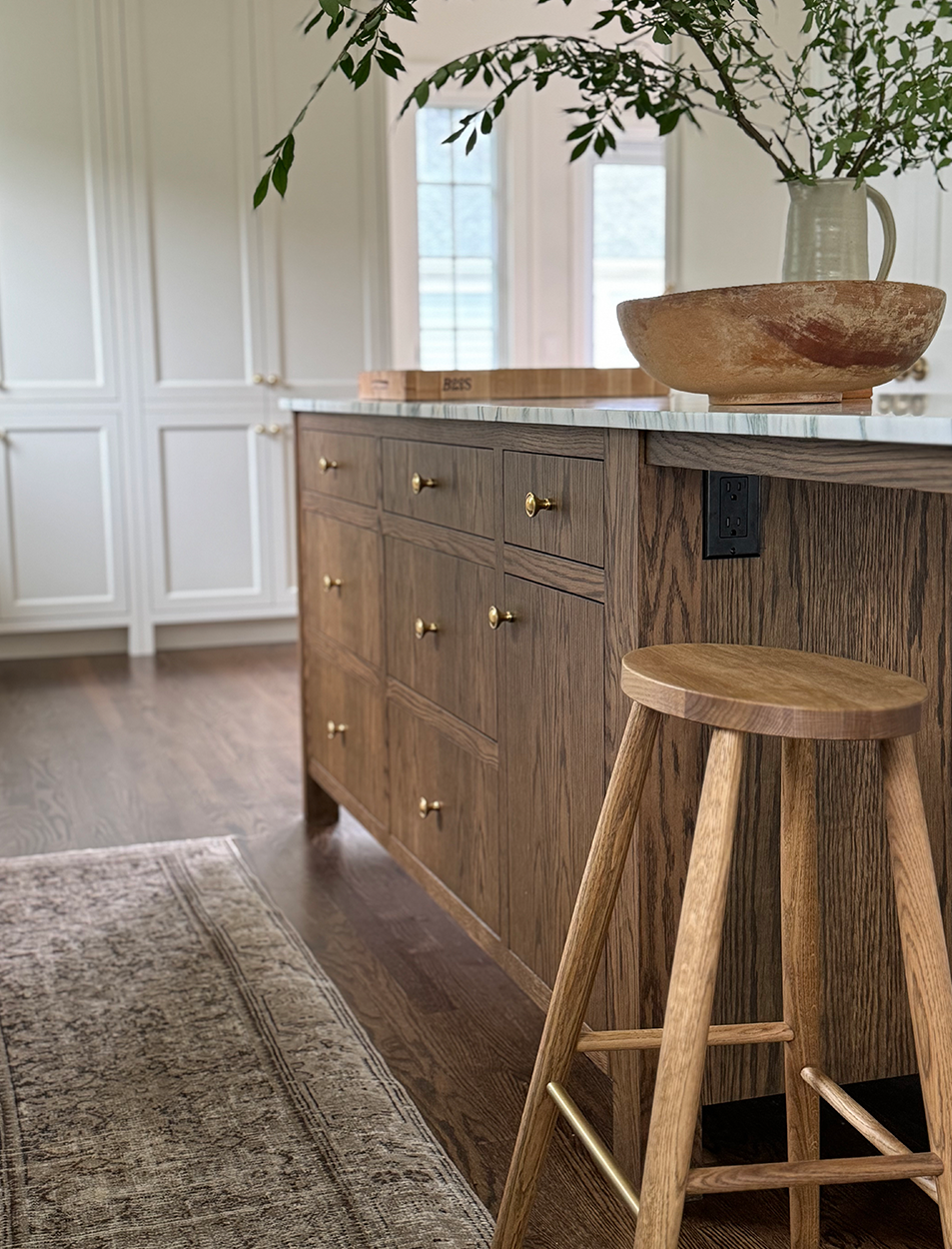 A wooden stool is sitting next to a wooden island in a kitchen.