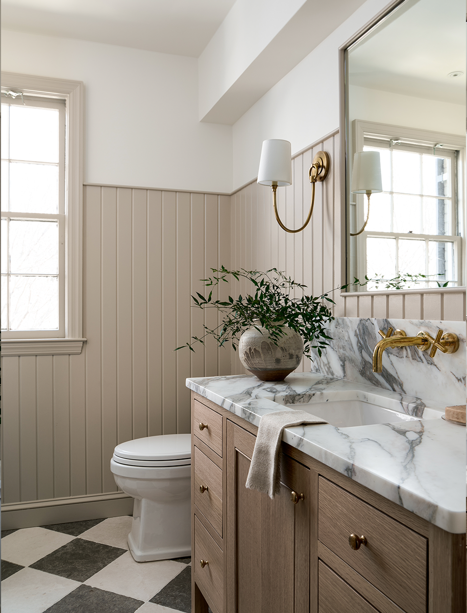 A bathroom with a toilet , sink , mirror and checkered floor.