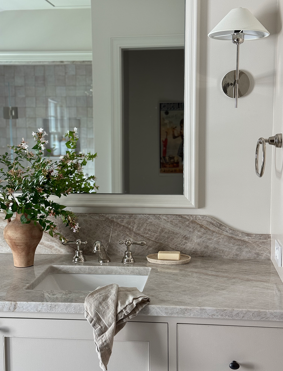 A bathroom sink with a vase of flowers on it and a mirror.
