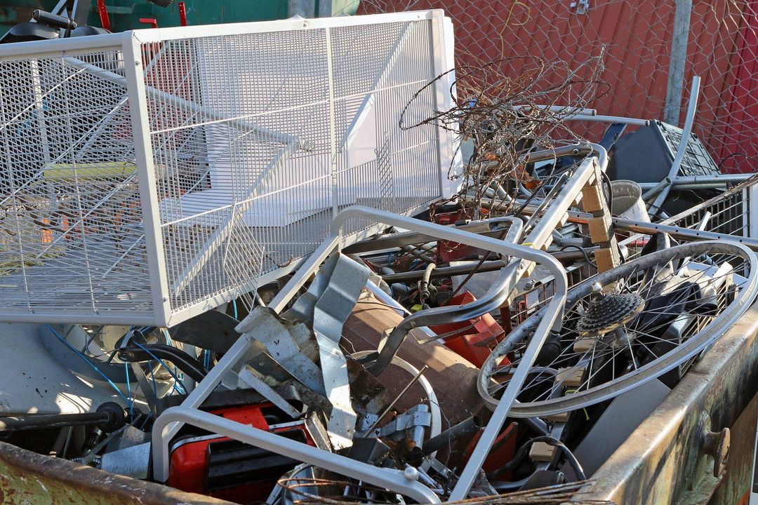 Pile of scrap metal, including a shopping cart, wheels, and various metal objects in a bin.