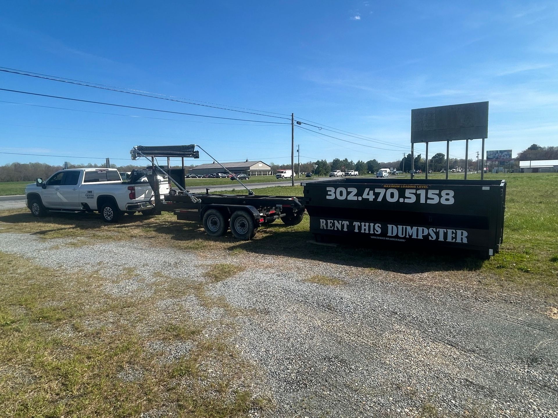 White truck with a dumpster on a trailer. The dumpster reads 