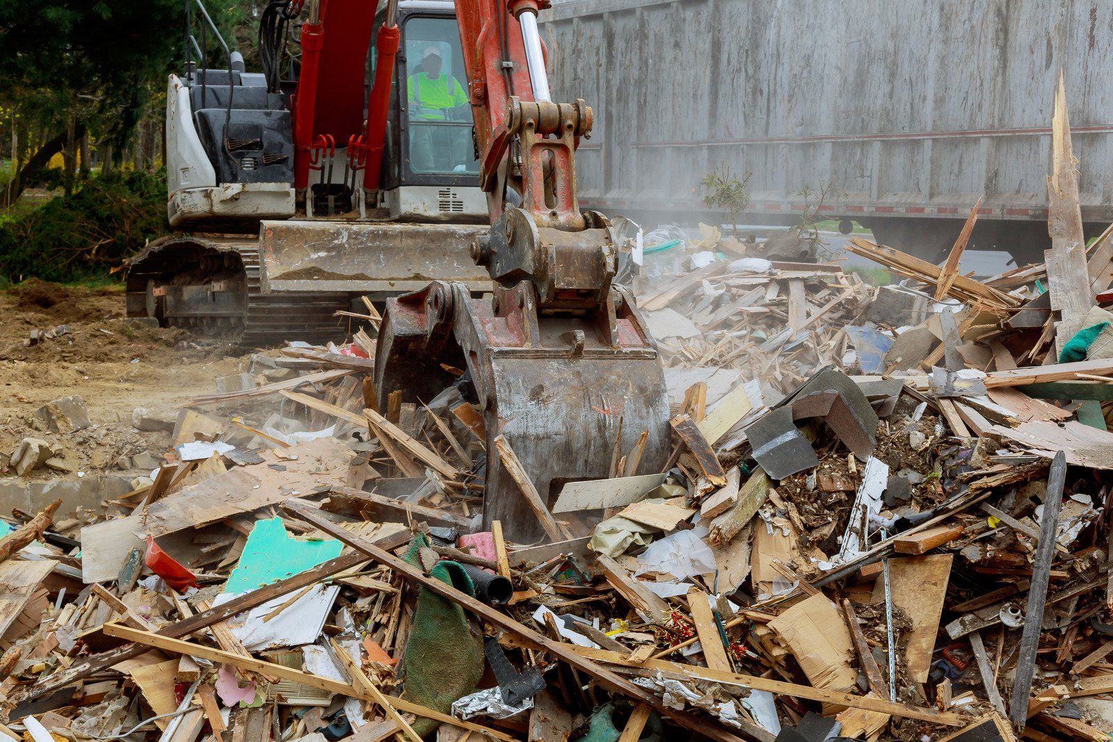 An excavator demolishes a building, scooping up debris, white cab, brown bucket.