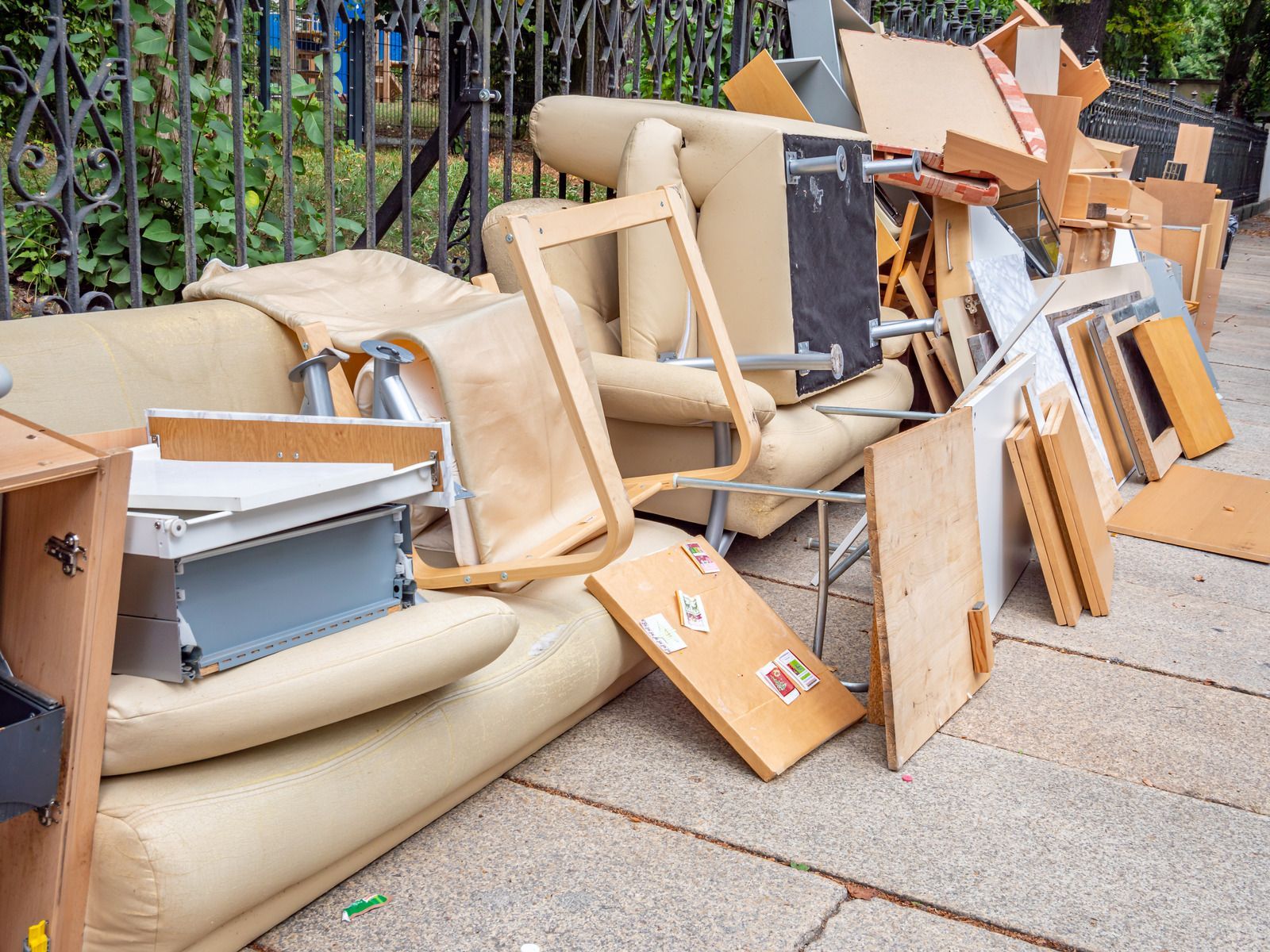 Pile of discarded furniture and debris on a sidewalk, including a sofa, chair, and wooden boards.
