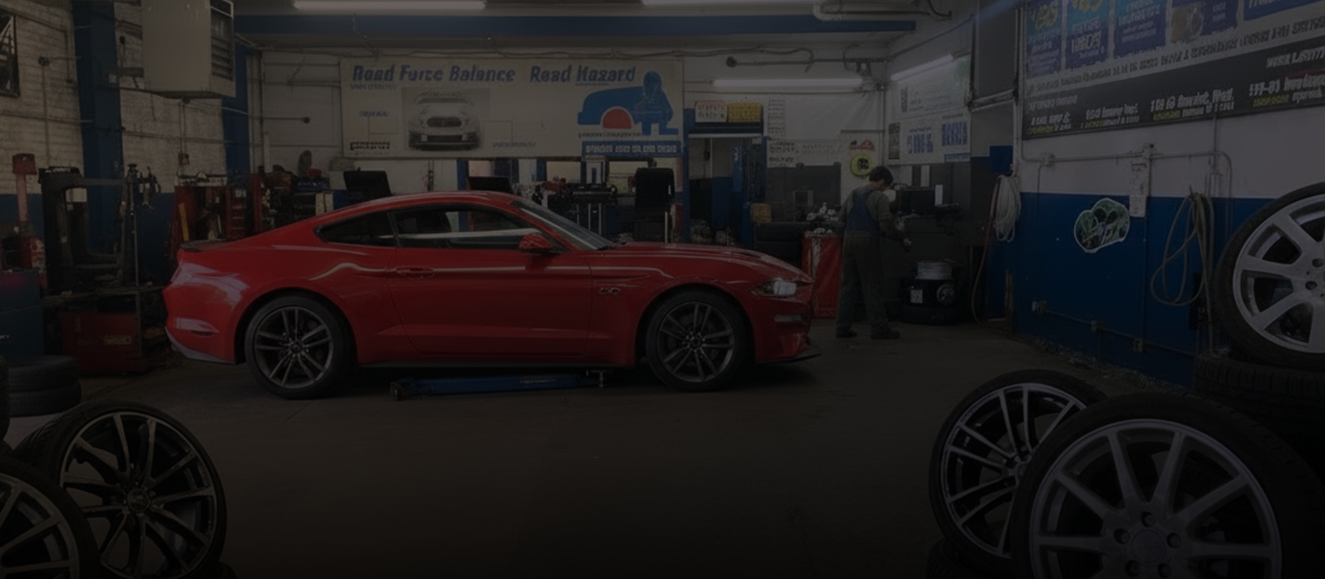 Red sports car in an auto shop garage, with people and wheels visible in the background. | 106 St Tire and Wheel