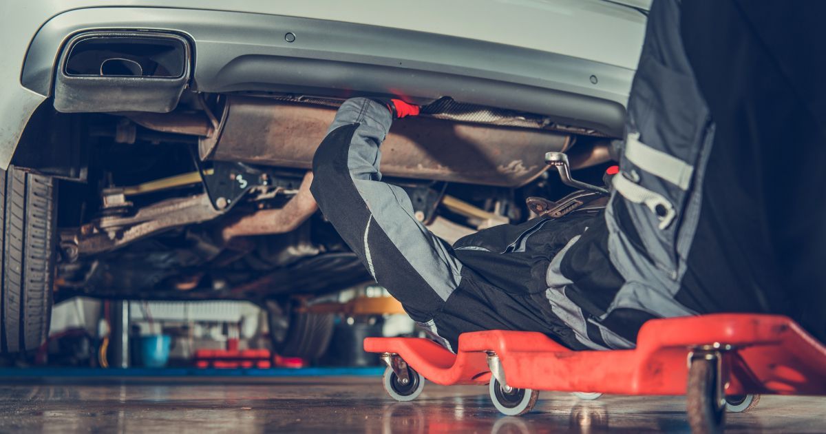 Mechanic working under a car on a red creeper in a garage | 106 St Tire and Wheel