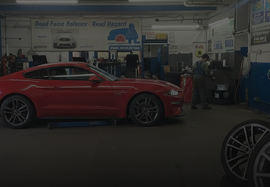 Red sports car in an auto repair shop with equipment and a wheel in the foreground. | 106 St Tire and Wheel