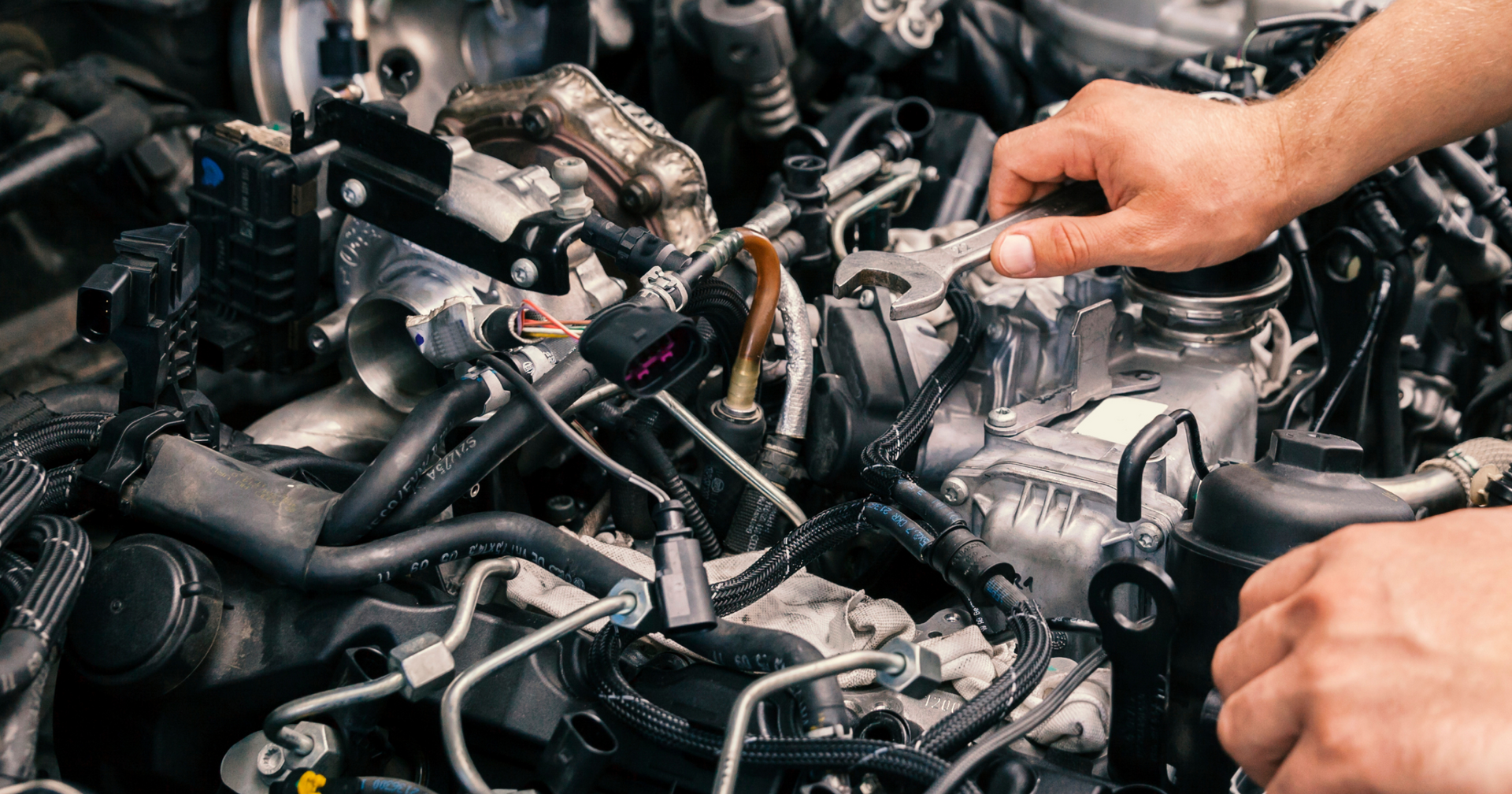 Mechanic working on a car engine with exposed components and tangled hoses | 106 St Tire and Wheel