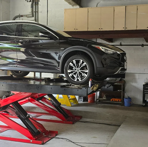 Black SUV raised on a red hydraulic lift inside an auto garage | 106 St Tire and Wheel